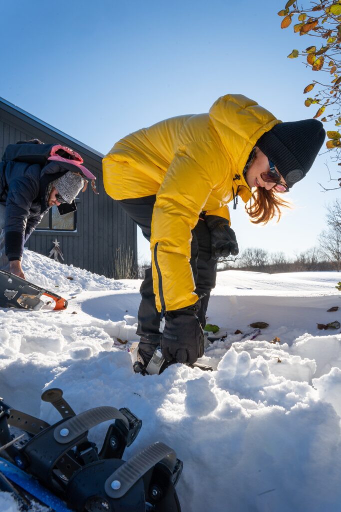 Snowshoe and Wine Women in yellow jacket bending over to fasten snowshoes