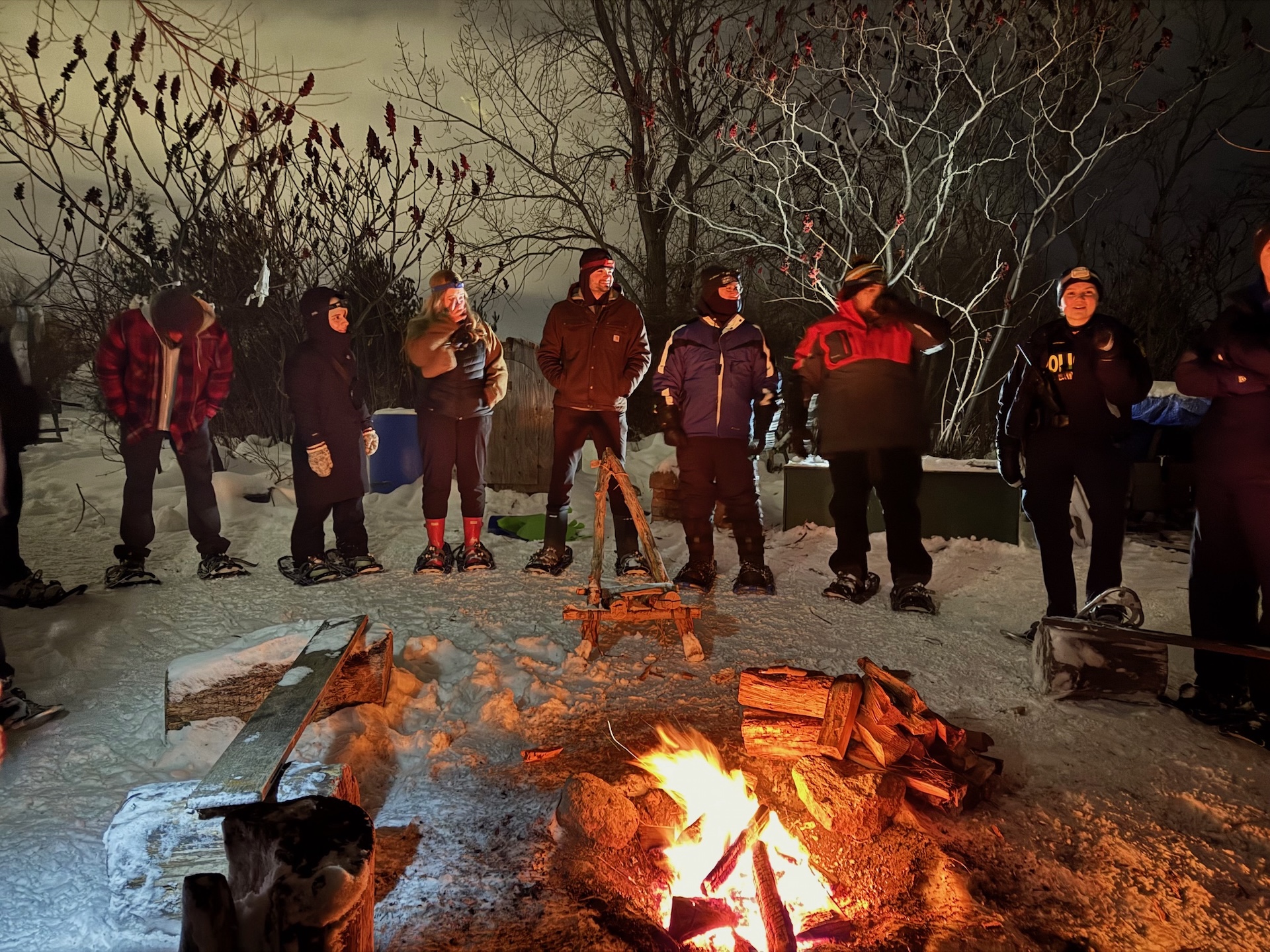 Group of people standing around a bonfire at night in winter