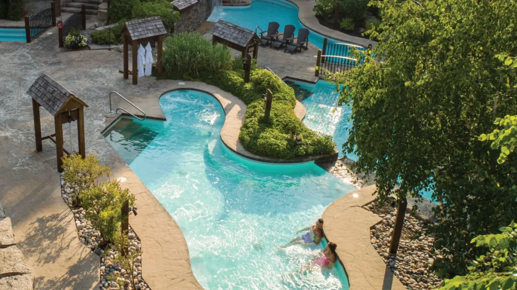 26-thermal-journey-page-2350-x-1320 Aerial view of outdoor pool and lounging area at Scandinave spa. Pool surrounded by trees on a sunny day.