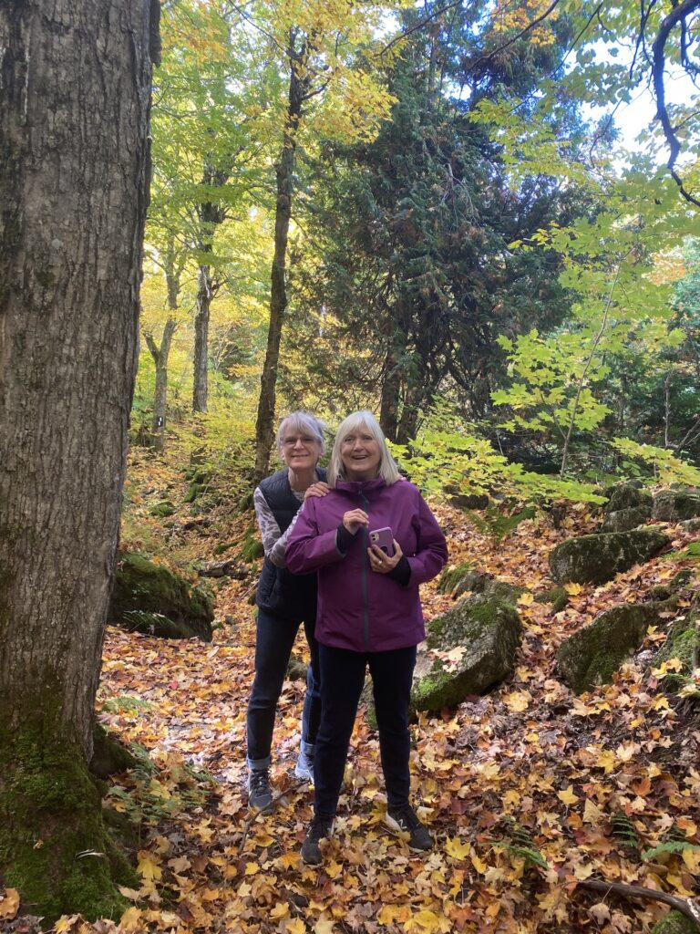 Fall Hike3 2 ladies smiling on a hike in the forest with the floor covered in leaves
